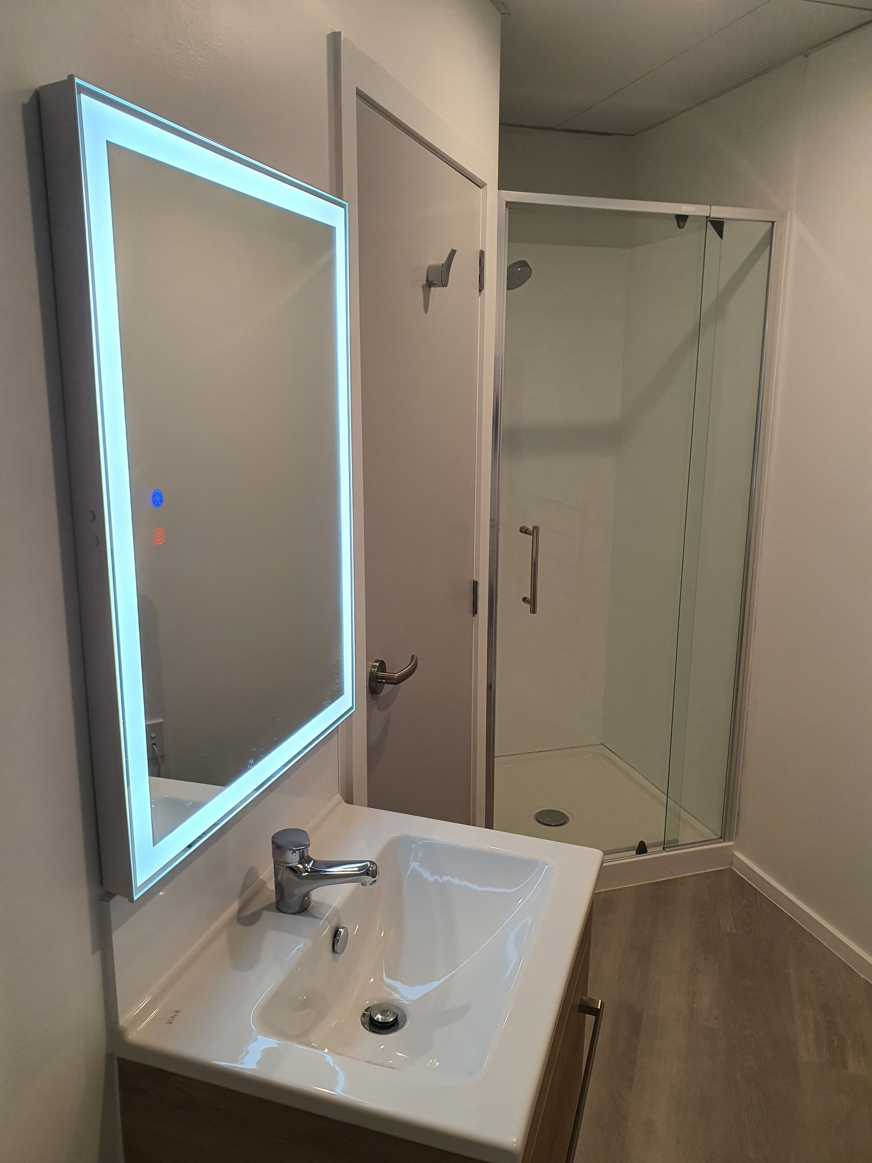 A bathroom with a white sink, a mirror with LED lighting, and a glass shower enclosure.