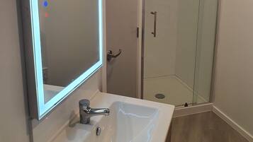 A bathroom with a white sink, a mirror with LED lighting, and a glass shower enclosure.