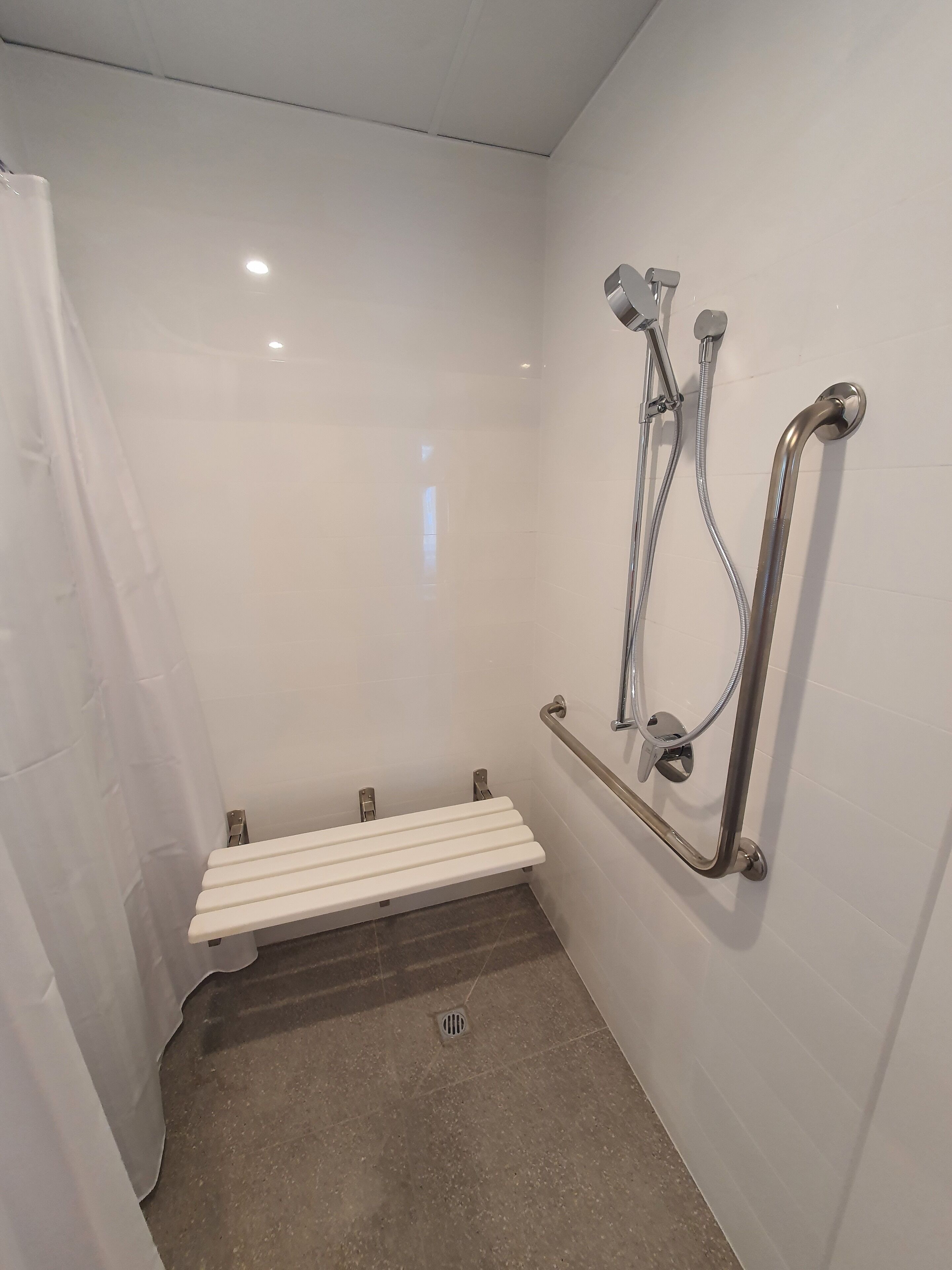A bathroom with a white shower enclosure, a white bench, and a grab bar.