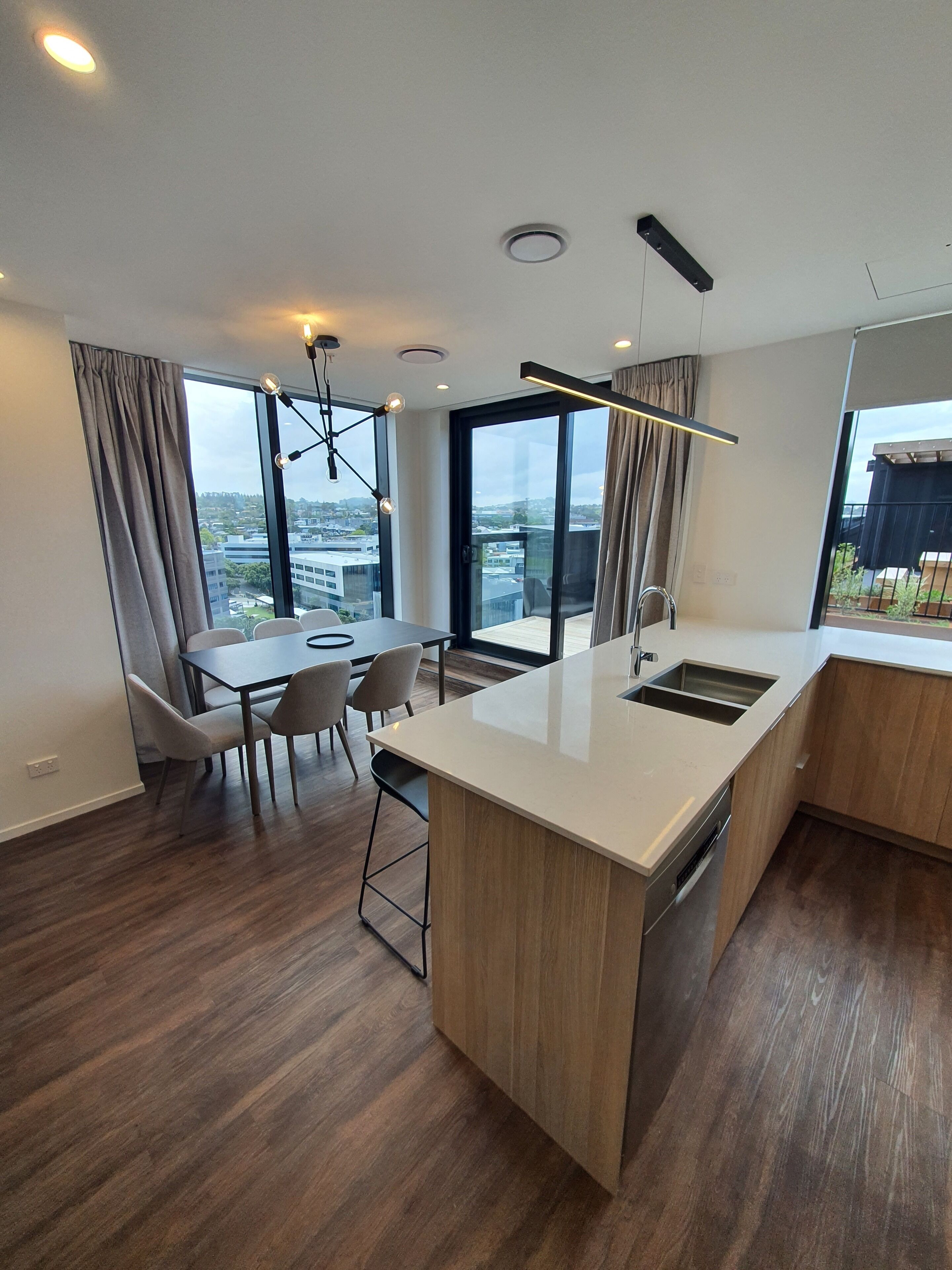A modern kitchen with a central island, a dining area with chairs, and large windows offering a city view.