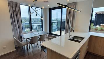 Una cocina moderna con una isla central, una zona de comedor con sillas y amplios ventanales con vistas a la ciudad.