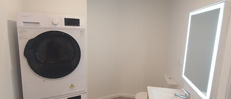 A compact bathroom with a washing machine, toilet, and a mirror with built-in lighting.