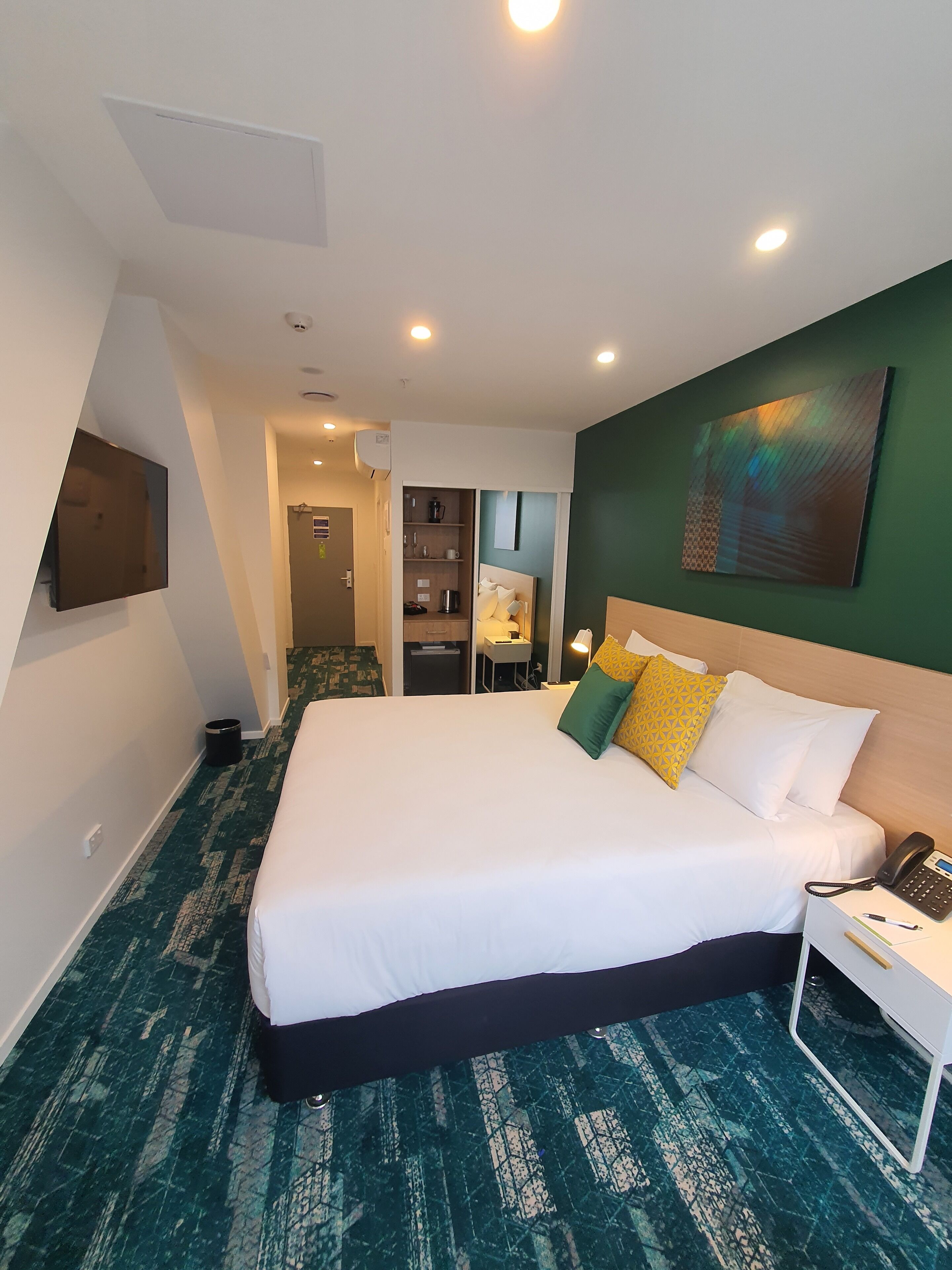 A hotel room with a large bed, a desk with a phone, and a painting on the wall.
