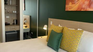 A hotel room with a bed, a desk, a wardrobe, and a painting on the wall.