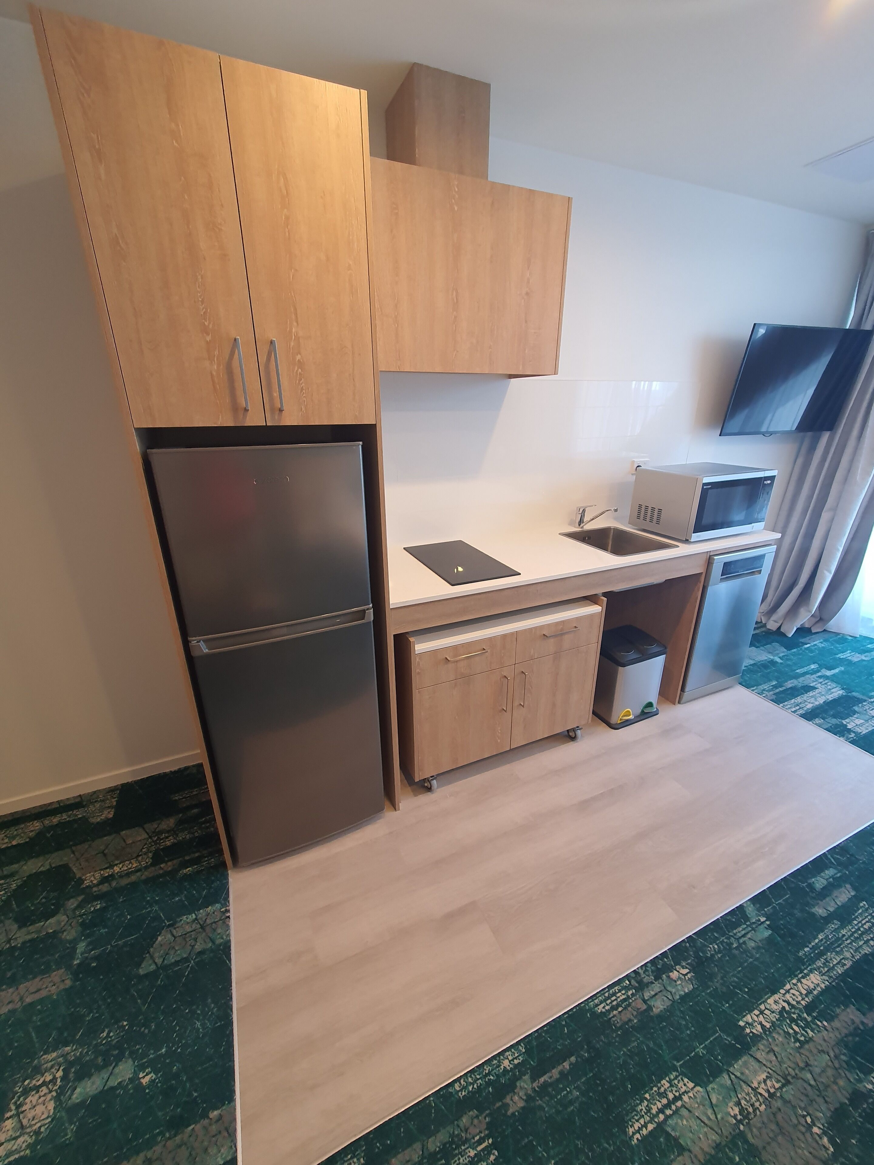 A compact kitchen with wooden cabinets, a built-in refrigerator, a microwave, and a sink.