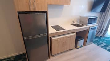 A compact kitchen with wooden cabinets, a built-in refrigerator, a microwave, and a sink.