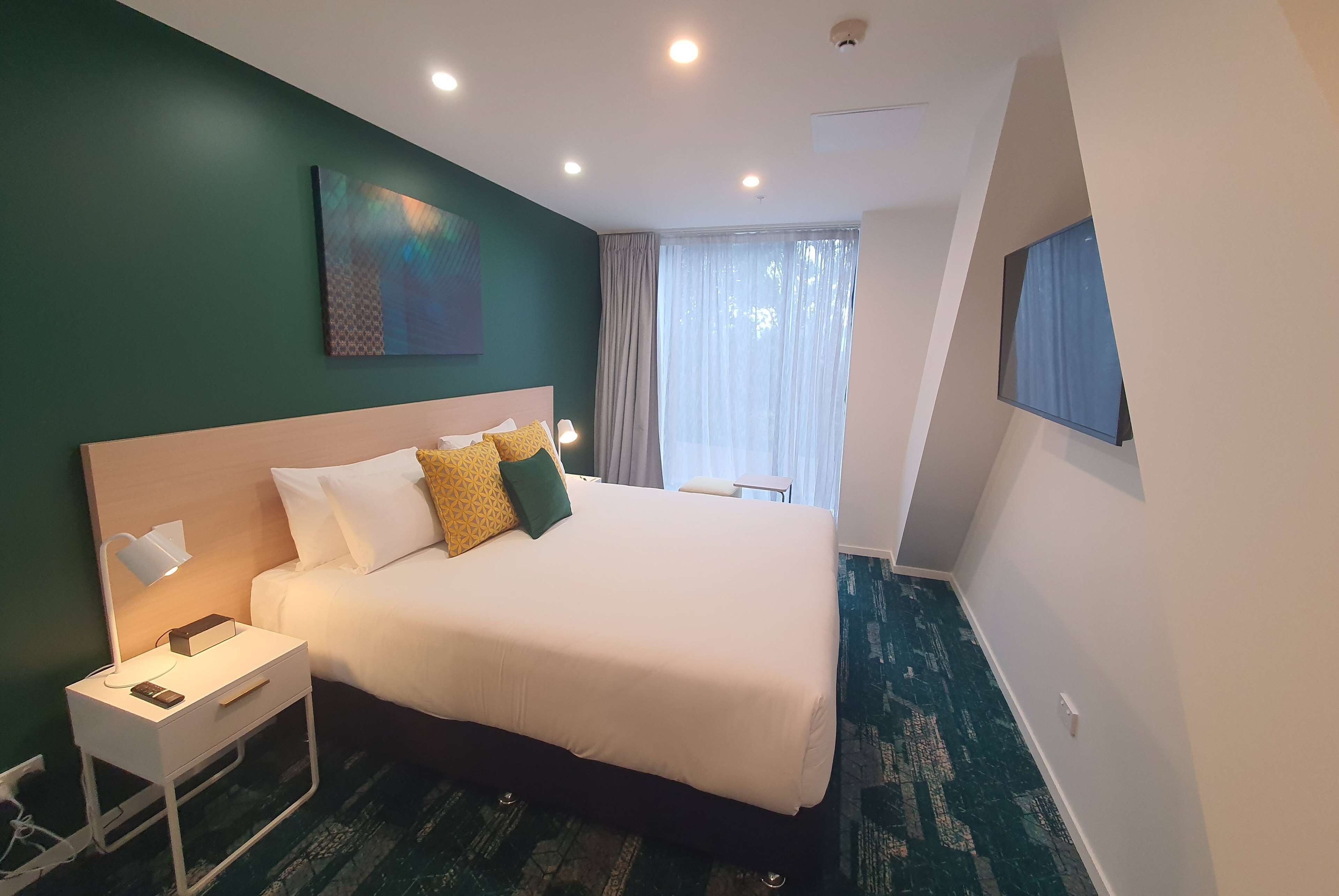 A neatly arranged hotel room with a large bed, bedside table, and a painting on the wall.