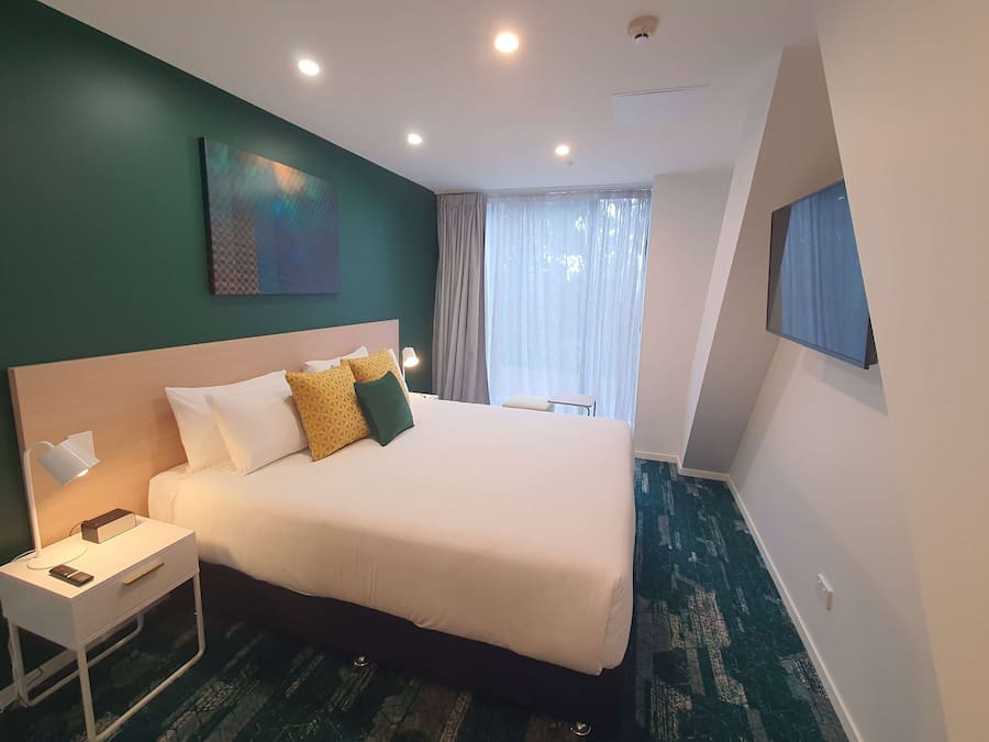 A neatly arranged hotel room with a large bed, bedside table, and a painting on the wall.