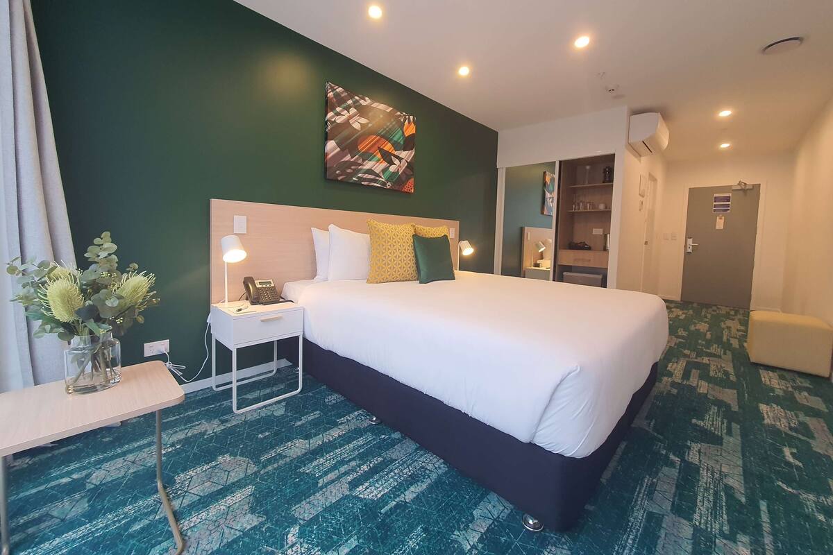 Ein Hotelzimmer mit einem großen Bett, einem Nachttisch, einer Lampe und einer kleinen Pflanze.