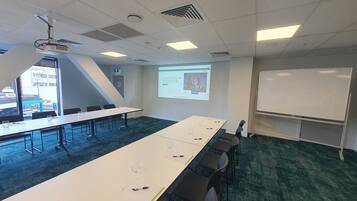 A conference room with a long table, chairs, a projector, and a whiteboard.
