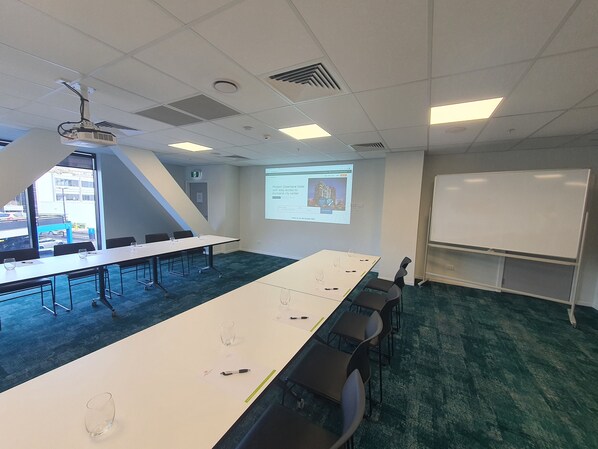 Un salón de conferencias con una larga mesa, sillas, un proyector y una pizarra.