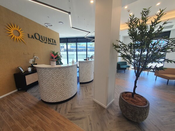 A reception area with a modern design, featuring a large logo on the wall, a reception desk, and a potted plant. - La Quinta By Wyndham Ellerslie Auckland (Auckland)