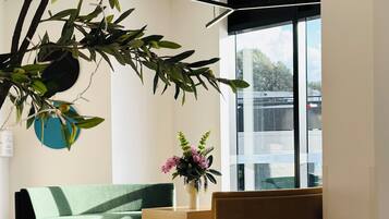 Um interior moderno com um sofá verde, uma mesa de centro de madeira e uma cadeira marrom. Uma janela grande oferece vista para o exterior.