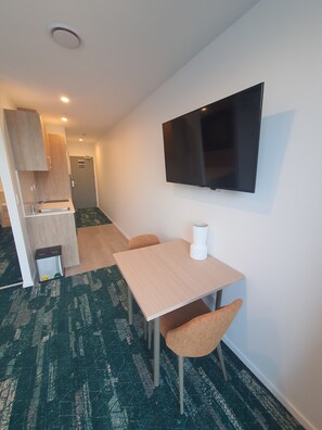 A compact hotel room with a kitchenette, a flat-screen TV mounted on the wall, a small table with two chairs, and a trash bin. - La Quinta By Wyndham Ellerslie Auckland (Auckland)