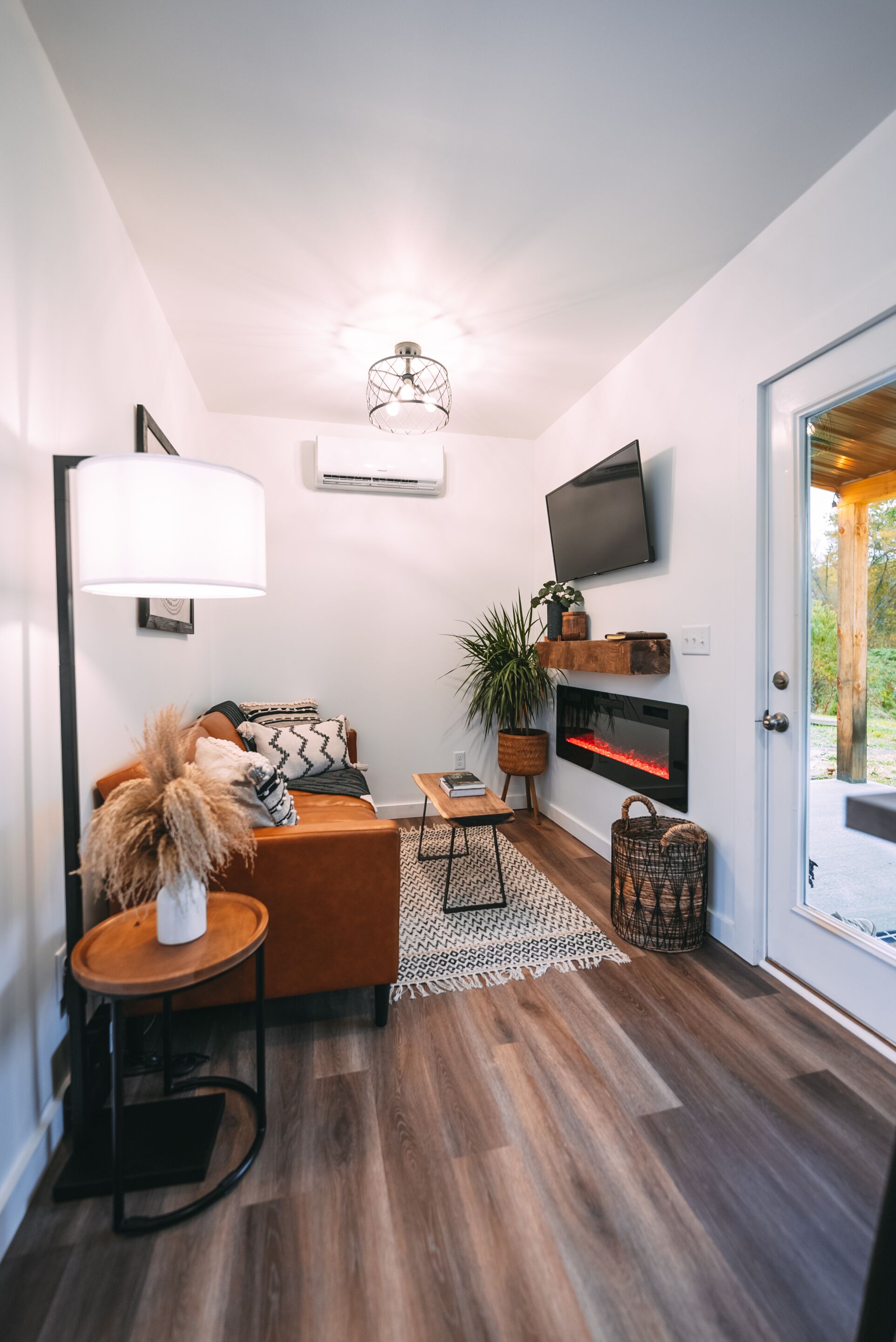 Una sala de estar moderna con un sofá, una mesa de centro, una chimenea, un televisor montado en la pared y una puerta que da al exterior.