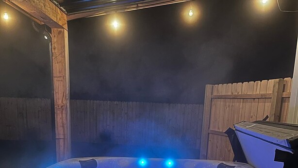 Un bain à remous doté de lumières LED bleues, entouré d’une terrasse en bois et d’une clôture en bois.
