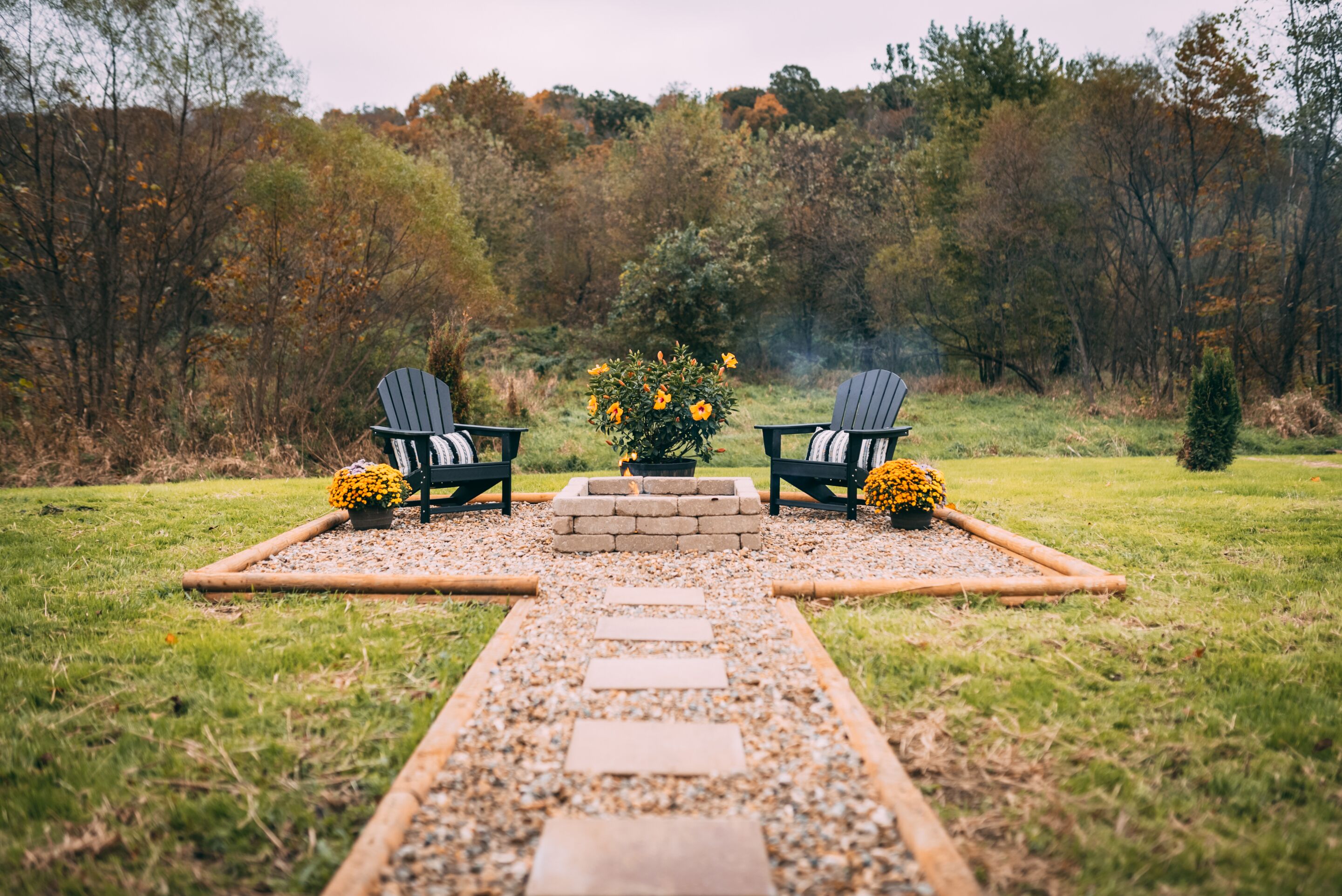 A garden pathway leading to a seating area with two Adirondack chairs and a central fire pit.
