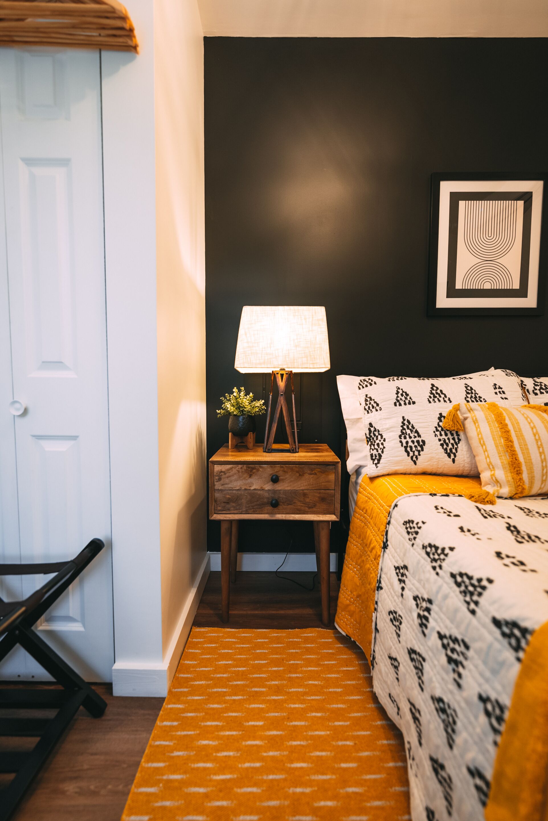 Un dormitorio con cama, mesita de noche, lámpara y un cuadro en la pared.