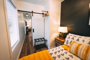 Una camera da letto con un letto, un comodino, una lampada e vista sul corridoio.