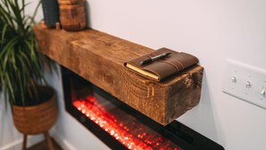 Une étagère en bois avec un carnet et un stylo, une plante en pot et une cheminée illuminée de lumière rouge.