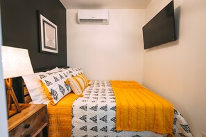 Een slaapkamer met een bed, nachtkastje, lamp, airconditioning en een lijst aan de muur.