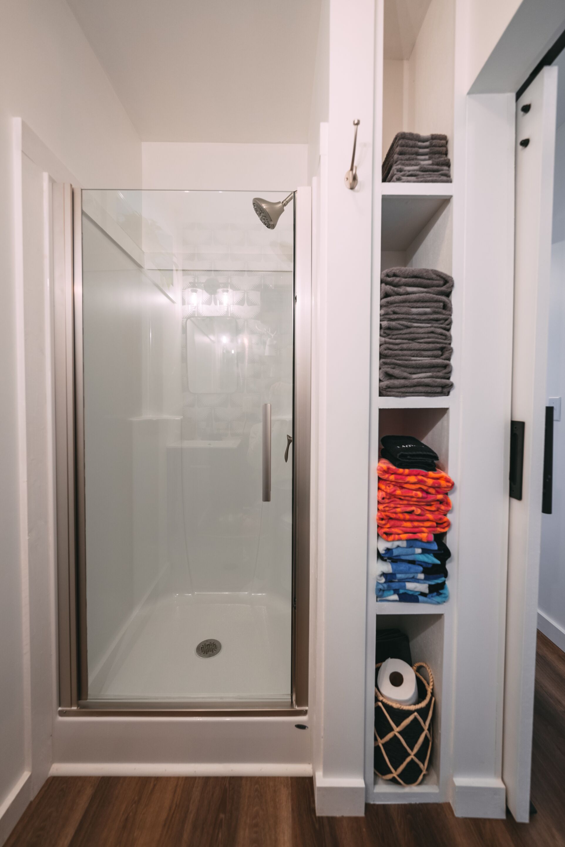 A glass-enclosed shower with a showerhead, a white door, and a wooden floor.