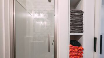 A glass-enclosed shower with a showerhead, a white door, and a wooden floor.