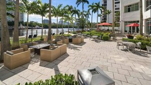 Un patio al aire libre con mobiliario, palmeras y vistas a un cuerpo de agua.