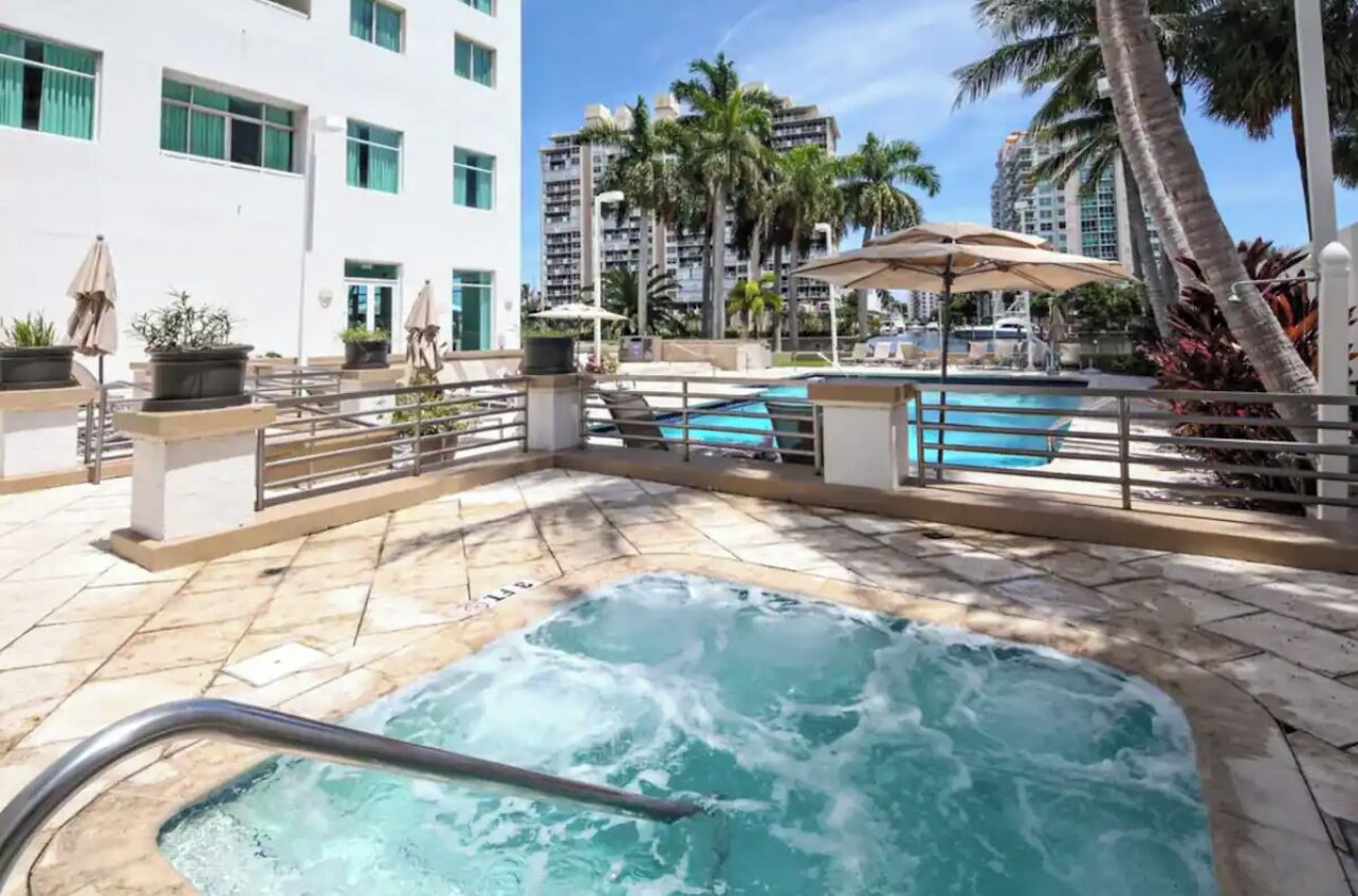 A hotel pool area with a hot tub, lounge chairs, and palm trees.