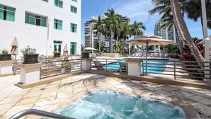 Zona de piscina de hotel con un jacuzzi, sillones de descanso y palmeras.