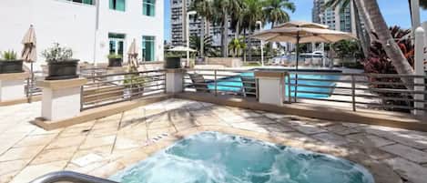 A hotel pool area with a hot tub, lounge chairs, and palm trees.