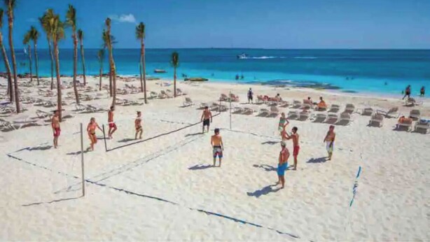 Una cancha de voleibol de playa con jugadores, palmeras y un cielo azul despejado.