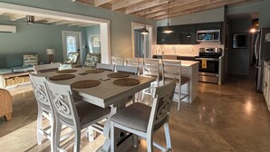 Uma sala de jantar ampla com uma mesa grande e cadeiras, uma cozinha com eletrodomésticos modernos e um ventilador de teto.