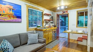 A cozy living room with a sofa, a coffee table, and a kitchen area with a wooden counter and cabinets. - Adorable A-Frame Cabin, Steps to Lake Cushman! (Hoodsport)