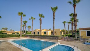 A swimming pool area with two pools, surrounded by palm trees and a fence. - Surmar - Apartment with pool in Cap d'Artrutx (Ciutadella de Menorca)