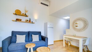A modern living room with a blue sofa, two wooden stools, a white desk, and a white refrigerator. - Surmar - Apartment with pool in Cap d'Artrutx (Ciutadella de Menorca)