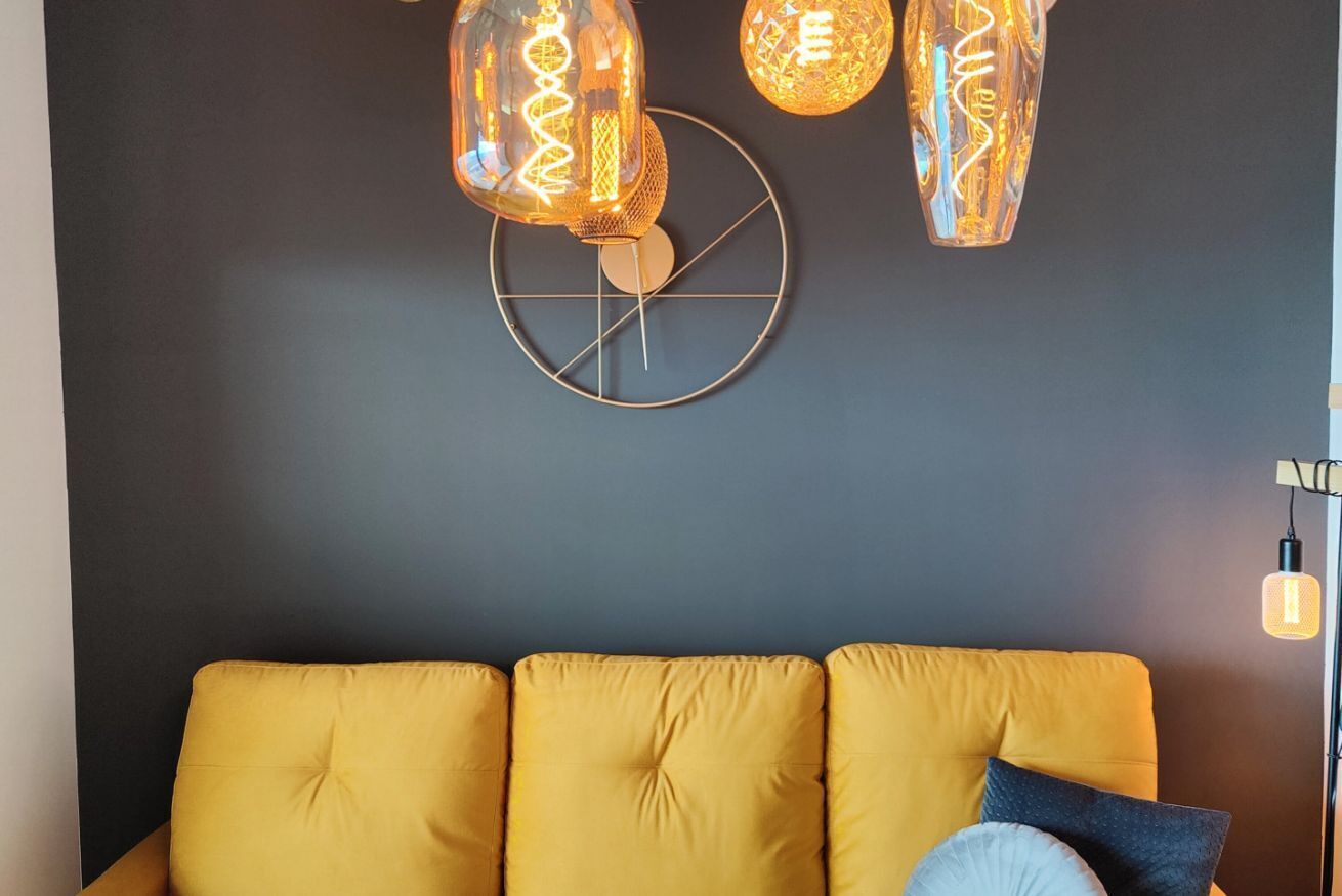 A modern living room with a yellow sofa, decorative wall art, and hanging light fixtures.