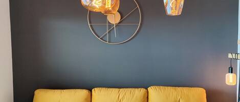A modern living room with a yellow sofa, decorative wall art, and hanging light fixtures.