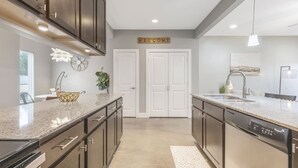 Une cuisine moderne avec des meubles de couleur sombre, un plan de travail en granit, un lave-vaisselle et un panneau d’accueil.