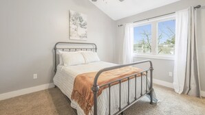 Une chambre à coucher avec un lit, un ventilateur de plafond, une fenêtre et un tableau au mur.