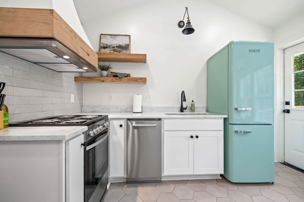 Una cocina con armarios blancos, estufa de acero inoxidable, lavavajillas y refrigerador color turquesa.