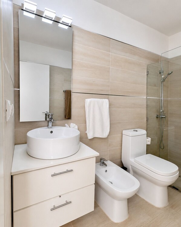 Une salle de bain moderne équipée d’un lavabo, de toilettes, d’un bidet et d’une douche à parois de verre.
