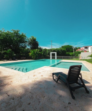 A swimming pool with a lounge chair and a white structure in the background. - 2JA Management Group - White Hill Condos (Sosúa)