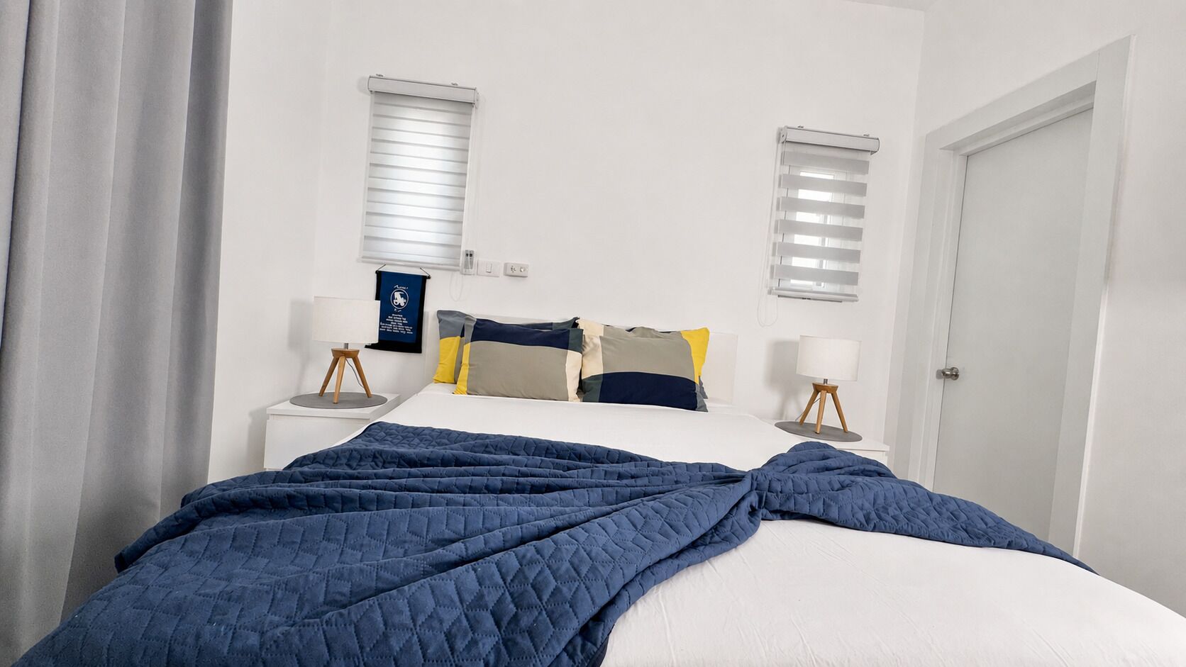 Un dormitorio con cama, dos mesitas de noche, una lámpara y una puerta.