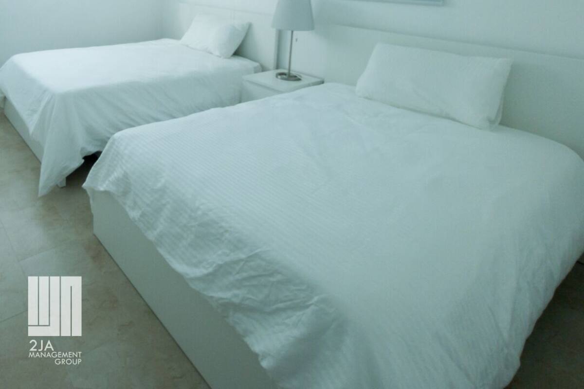 A hotel room with two beds, a ceiling fan, and two windows with blinds.