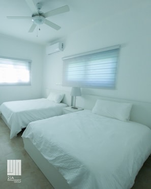 A hotel room with two beds, a ceiling fan, and two windows with blinds.