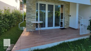 Un edificio moderno con fachada de piedra, terraza de madera y puerta de cristal que da a un espacio cubierto.