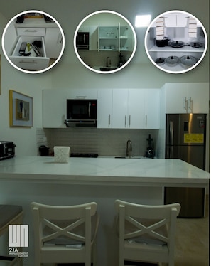 A modern kitchen with white cabinets, a central island, and a built-in microwave. - 2JA Management Group - White Hill Condos (Sosúa)
