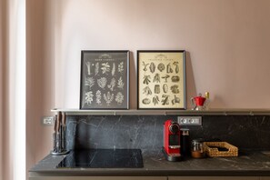A kitchen with a marble countertop, a coffee machine, and two framed botanical prints above the counter.