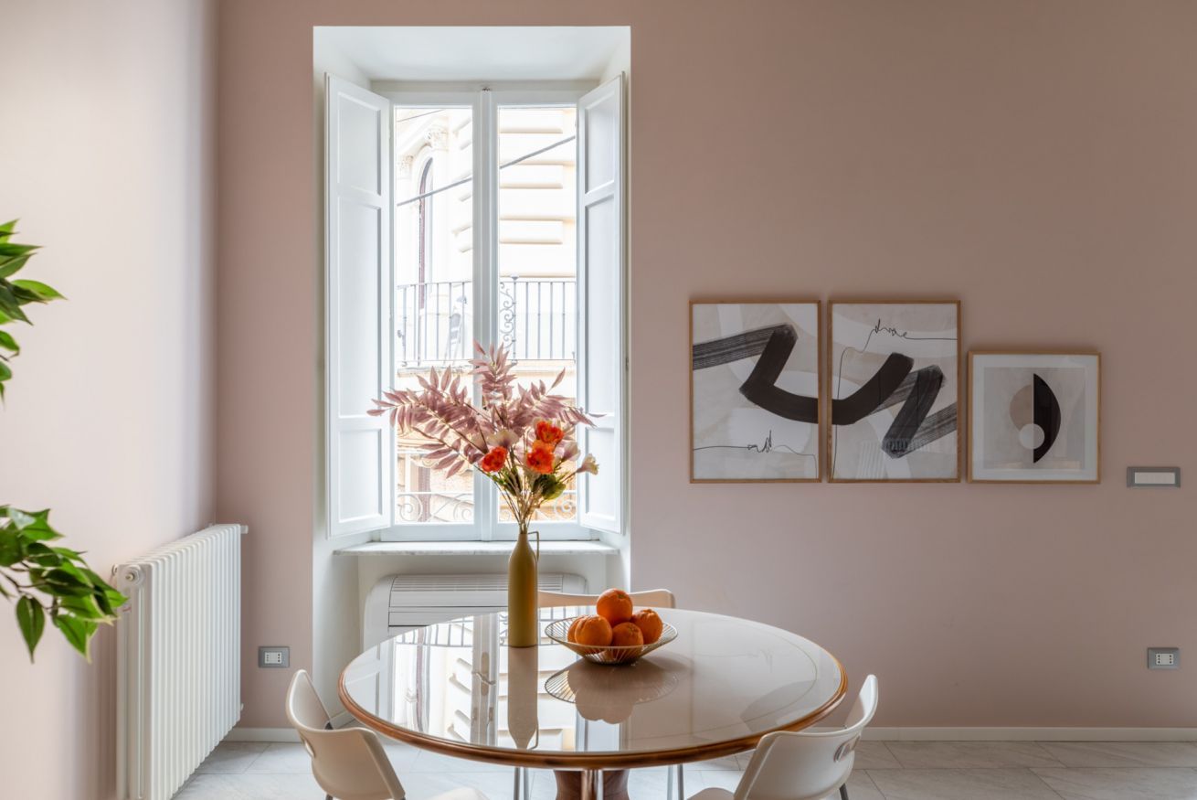 A dining area with a round table, chairs, a vase with flowers, and framed artwork on the wall.